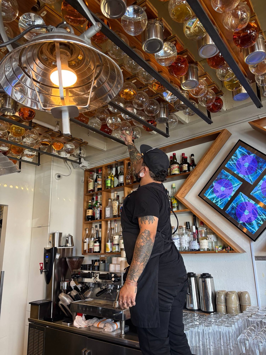 Round glass bottles hanging from racks in the ceiling above the bar at the Interval, a bartender reaching up for one
