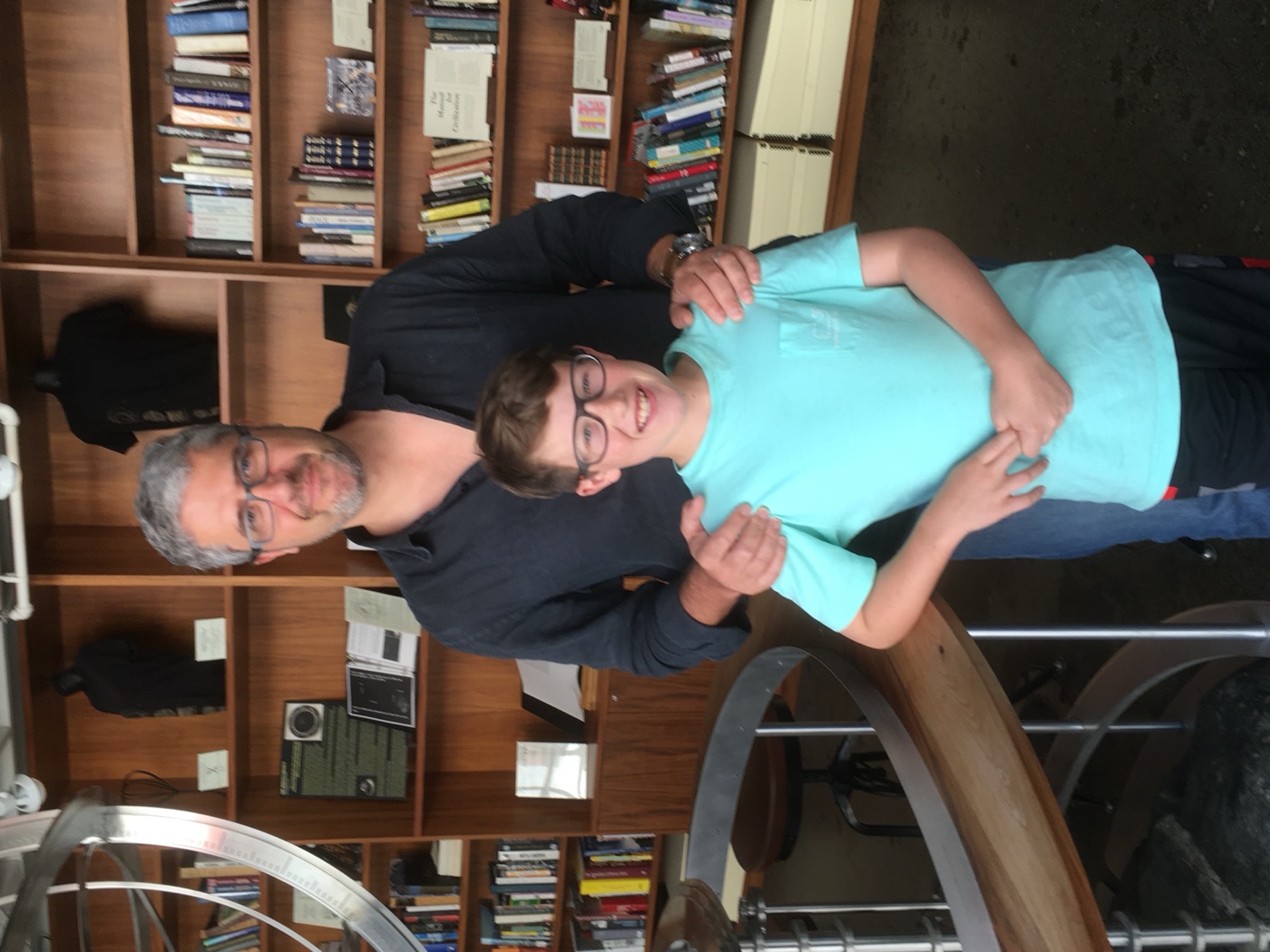 A man and a boy in a turquoise T-shirt stand in front of the bookshelves at the Interval